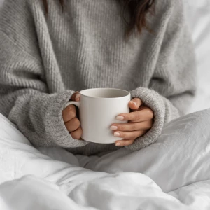 A cozy morning in bed with a woman wearing a soft gray sweater,...