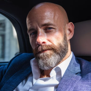 Refine the appearance of a bald man with a beard, sitting in a c...
