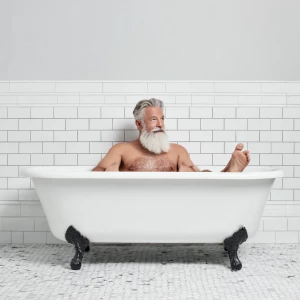 A bodybuilder man is sitting in an old-style bathtub that is whi...