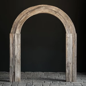 A wooden archway, centered in the image. The arch is made from beautiful vintage barndoor wood.   The archway has a smooth, semi-circular shape and shows the nails and slight wear of the weathered barn wood.  The wood has a grey, beige weathered color with lighter, streaky highlights.  The interior of the archway is completely black. The archway sits atop a natural vintage cobble stones. The background is a plain,black.The overall style is rustic, minimalist, and natural, evoking a sense of warmth and organic beauty. The lighting is even, casting no distinct shadows within the image, which enhances the focus on the wood texture and its details. The perspective is straight-on, looking directly at the archway.