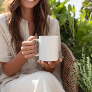 A woman sitting on a patio chair surrounded by green plants, hol...