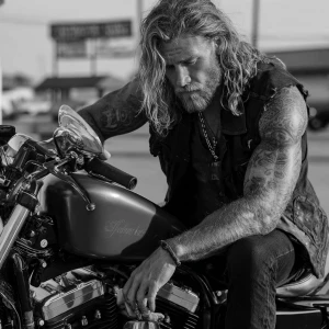 The image shows a muscular bodybuilder man with a tattooed arm s...