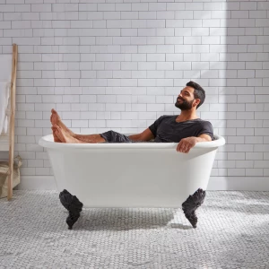 A man is sitting in a old style bathtub that is white large adul...