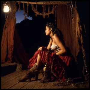 A Wench clothes torn, squatting,  chained onto a breading block...