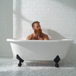 A bodybuilder man is sitting in a old style bathtub that is whit...