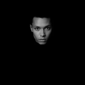 High-contrast monochromatic portrait with a single key light. Su...