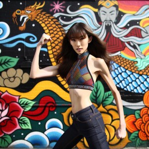 Athletic Thin skinny Attractive, Asian teenage girl, long brown hair and bangs, wearing tight skinny jeans and a halter top paint marks on her clothing, heroic pose Asian graffiti background