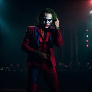 The Joker muscles fully made up on stage very dim lit with Harle...