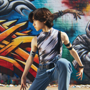 teenage girl, long brown hair and bangs, wearing tight skinny jeans and a halter top paint marks on her clothing, heroic pose Asian graffiti background, nearing on one knee