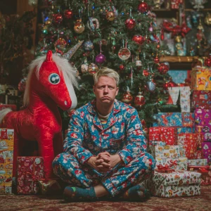 man sitting near Christmas tree looking into the camera in Chris...