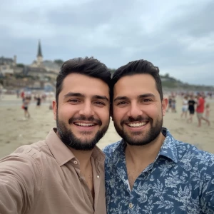 This image shows two men posing for a selfie together on a beach...