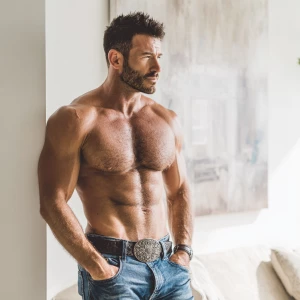 The image captures a strong, muscular man standing in a bright,...